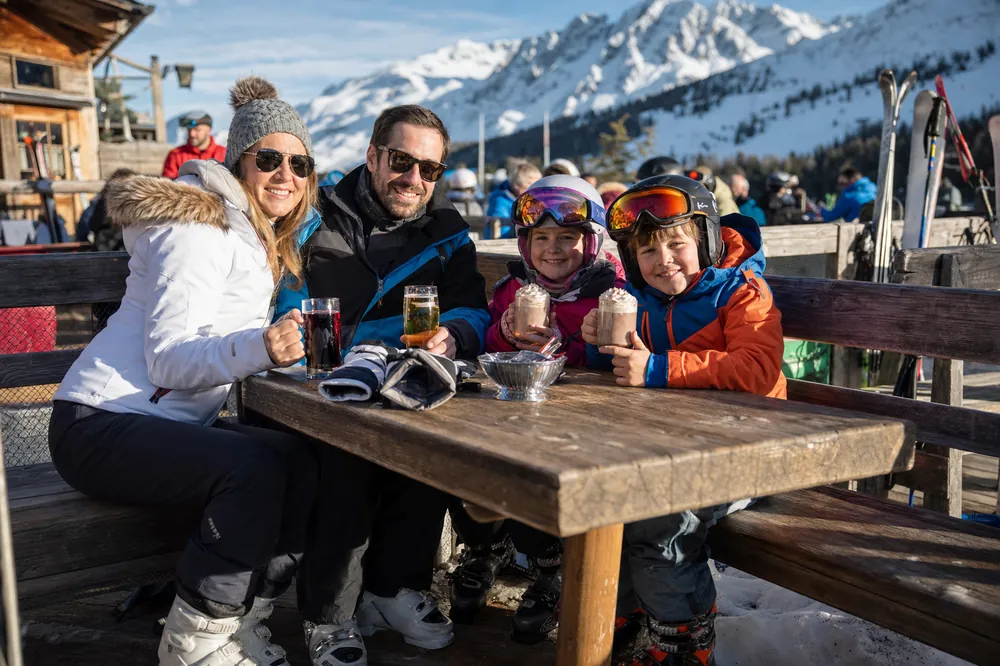 Familie mit heißer Schokolade auf einer sonnigen Terrasse an der Piste